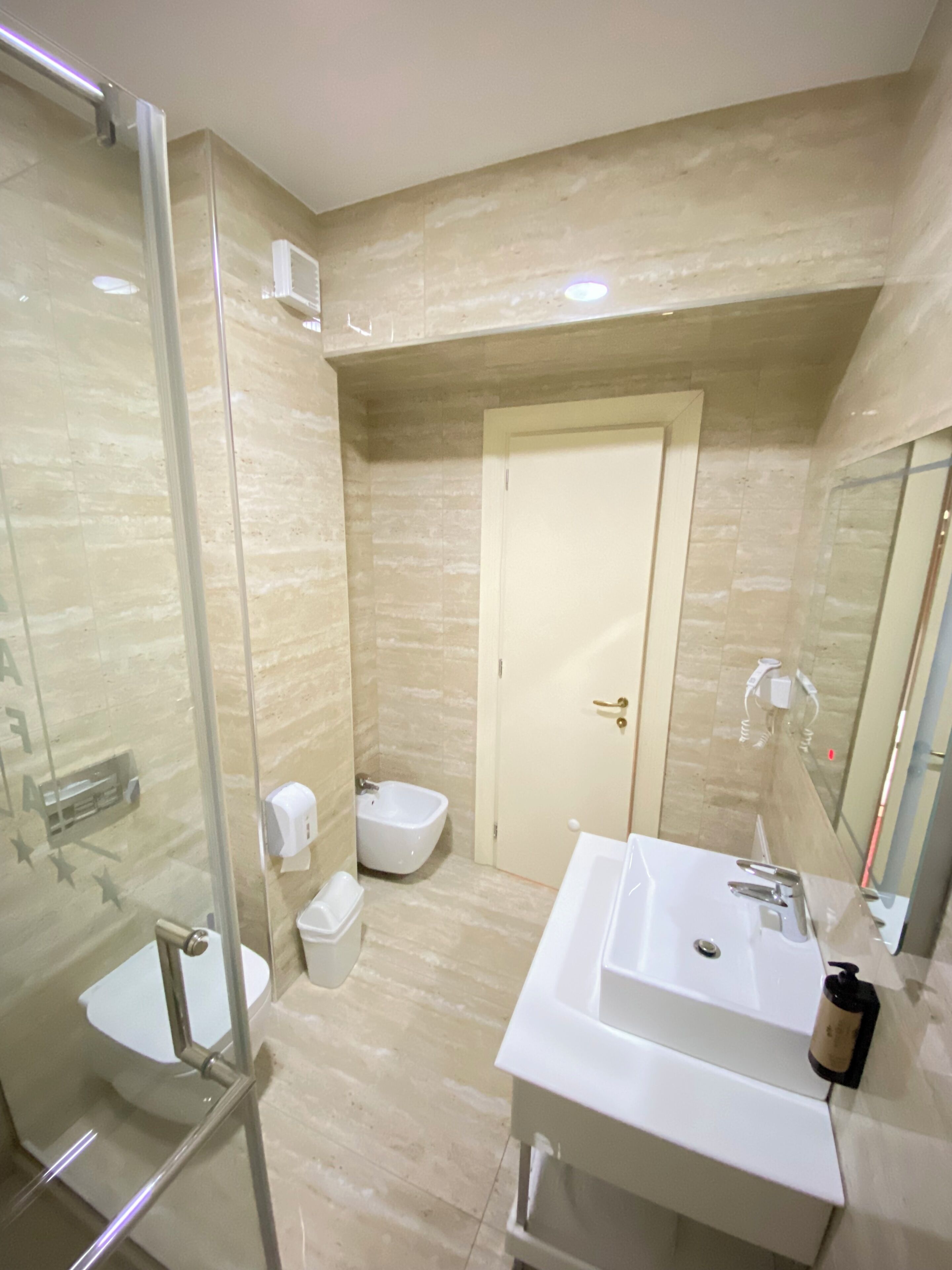 A bathroom with a glass shower enclosure, a toilet, a bidet, and a sink with a mirror.
