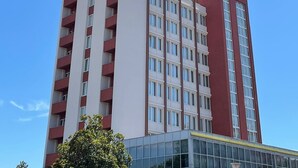 Ein mehrstöckiges Hotelgebäude mit roter und weißer Fassade, Balkonen auf jeder Etage und blauem Himmel im Hintergrund.