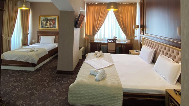 Ein Hotelzimmer mit zwei Betten, einem Schreibtisch, einem Sessel und einem großen Fenster mit Vorhängen.