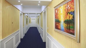 Ein Hotel-Flur mit blauem Teppich, weißem Zierleisten und einem großen Gemälde an der rechten Wand.