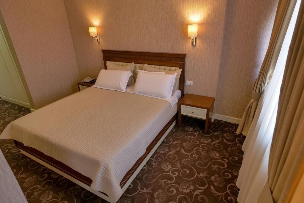 A hotel room with a large bed, two bedside tables, and wall-mounted lamps.