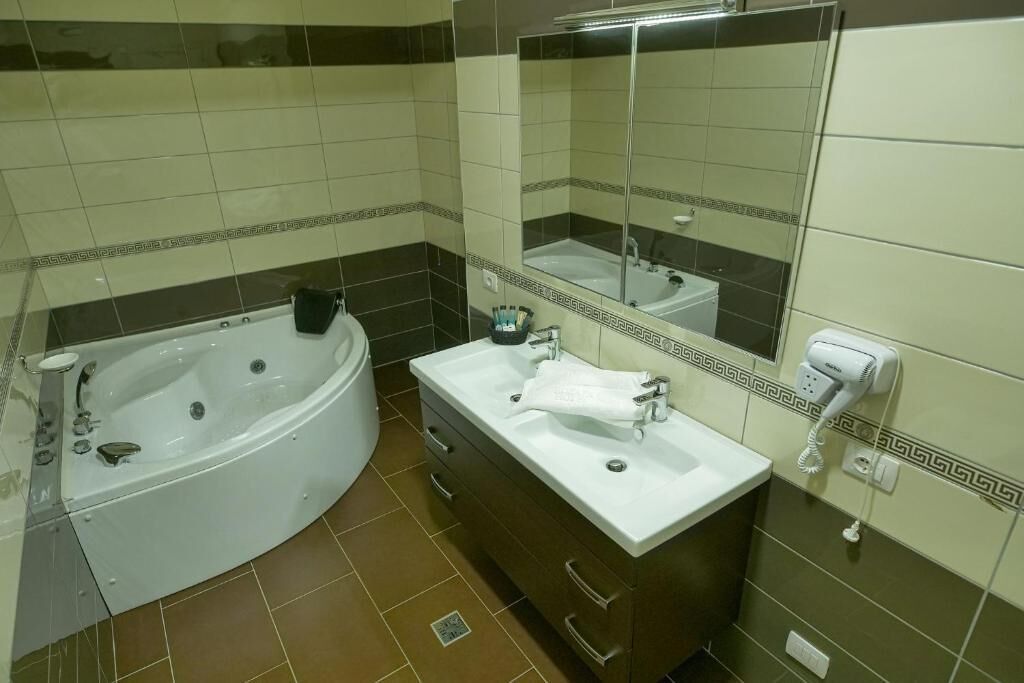 A bathroom with a bathtub, two sinks, a vanity, a mirror, and a hairdryer.