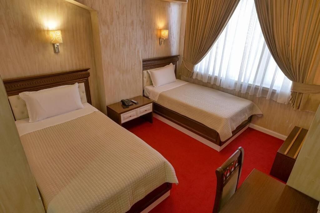 A hotel room with two beds, a red carpet, wooden headboards, and a window with curtains.
