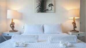Una cama bien hecha con sábanas blancas, dos mesitas de noche con lámparas, y un cuadro sobre la cama.