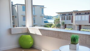 Un balcón con vistas a edificios y una masa de agua. Hay un jarrón verde y una pequeña mesa con una planta en maceta.