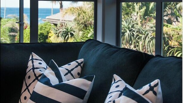 Una habitación con un ventanal grande que da a un paisaje tropical y al océano.