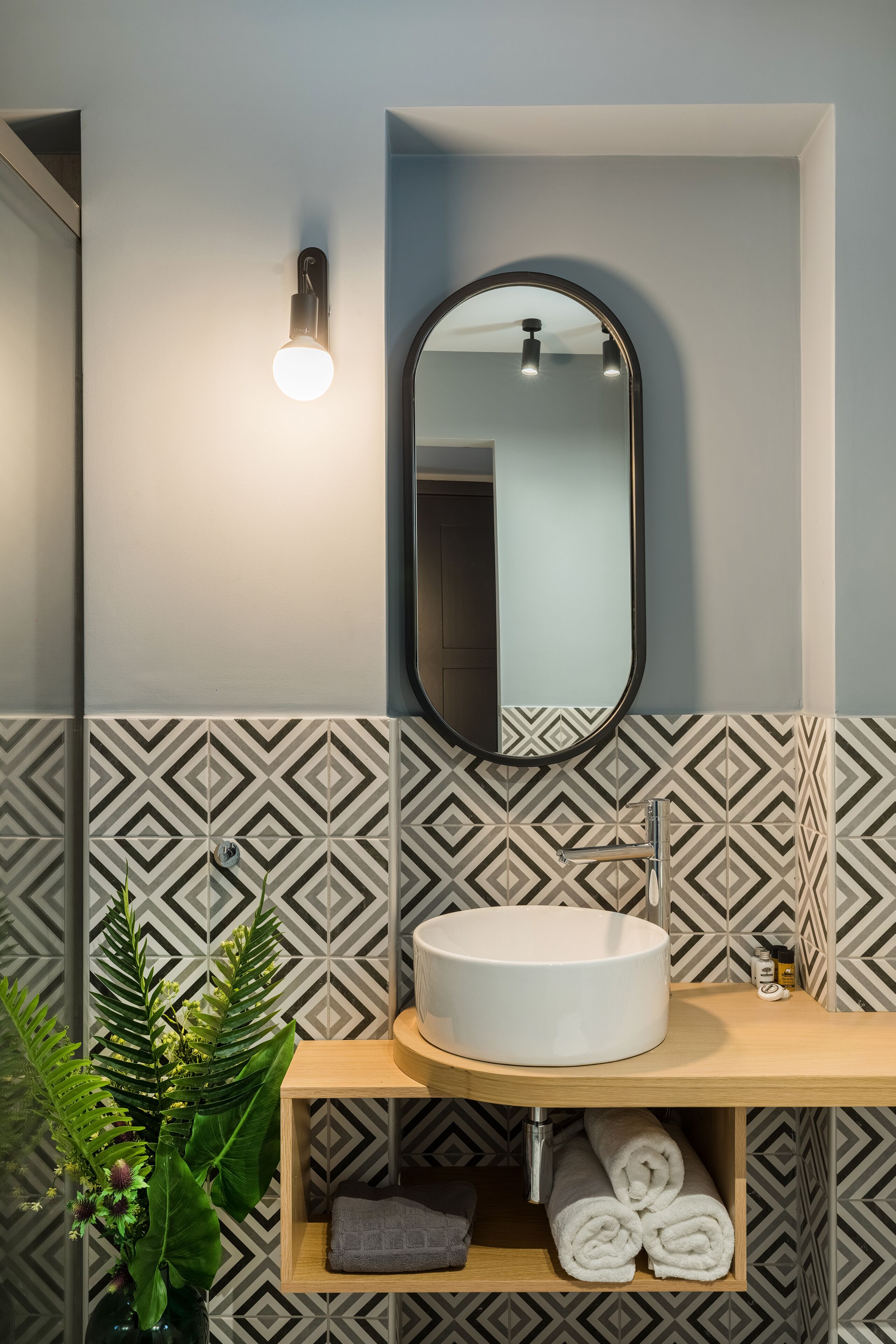 A bathroom with a round sink, a mirror, a wall-mounted light, and patterned tiles.