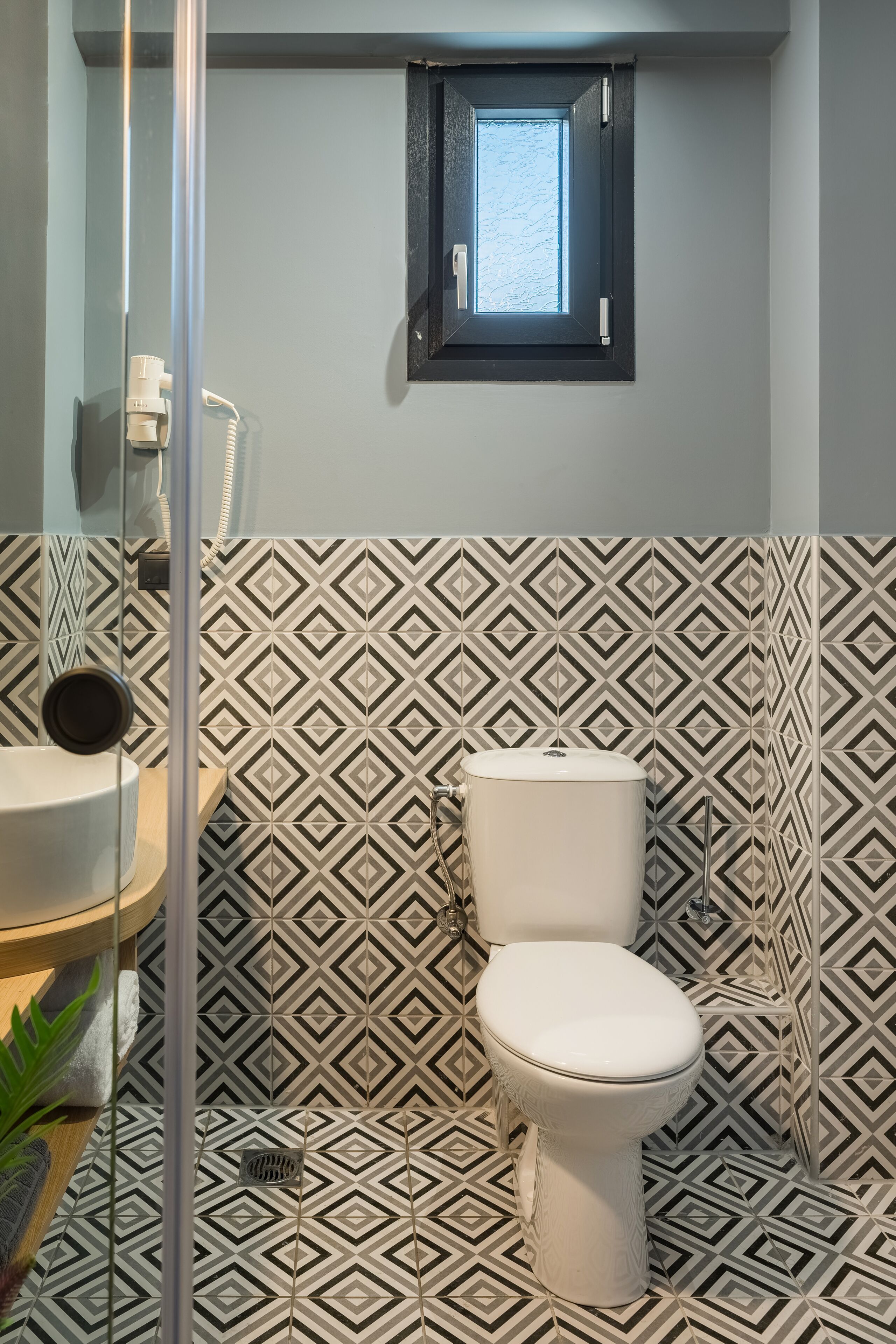 A bathroom with a geometric patterned tile wall, a toilet, a sink, and a window with a view.