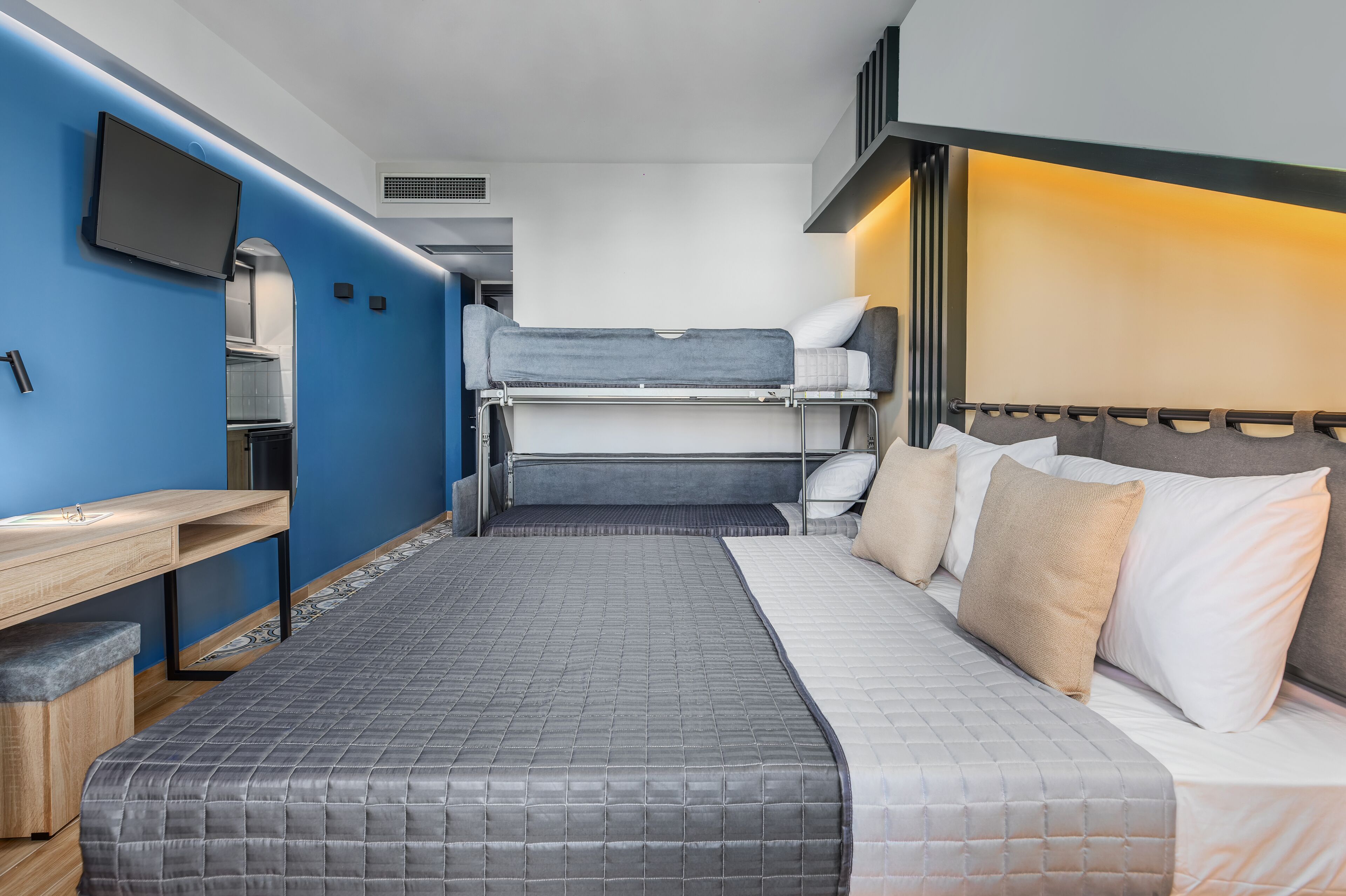 A compact hotel room with a bunk bed, a desk, and a television.