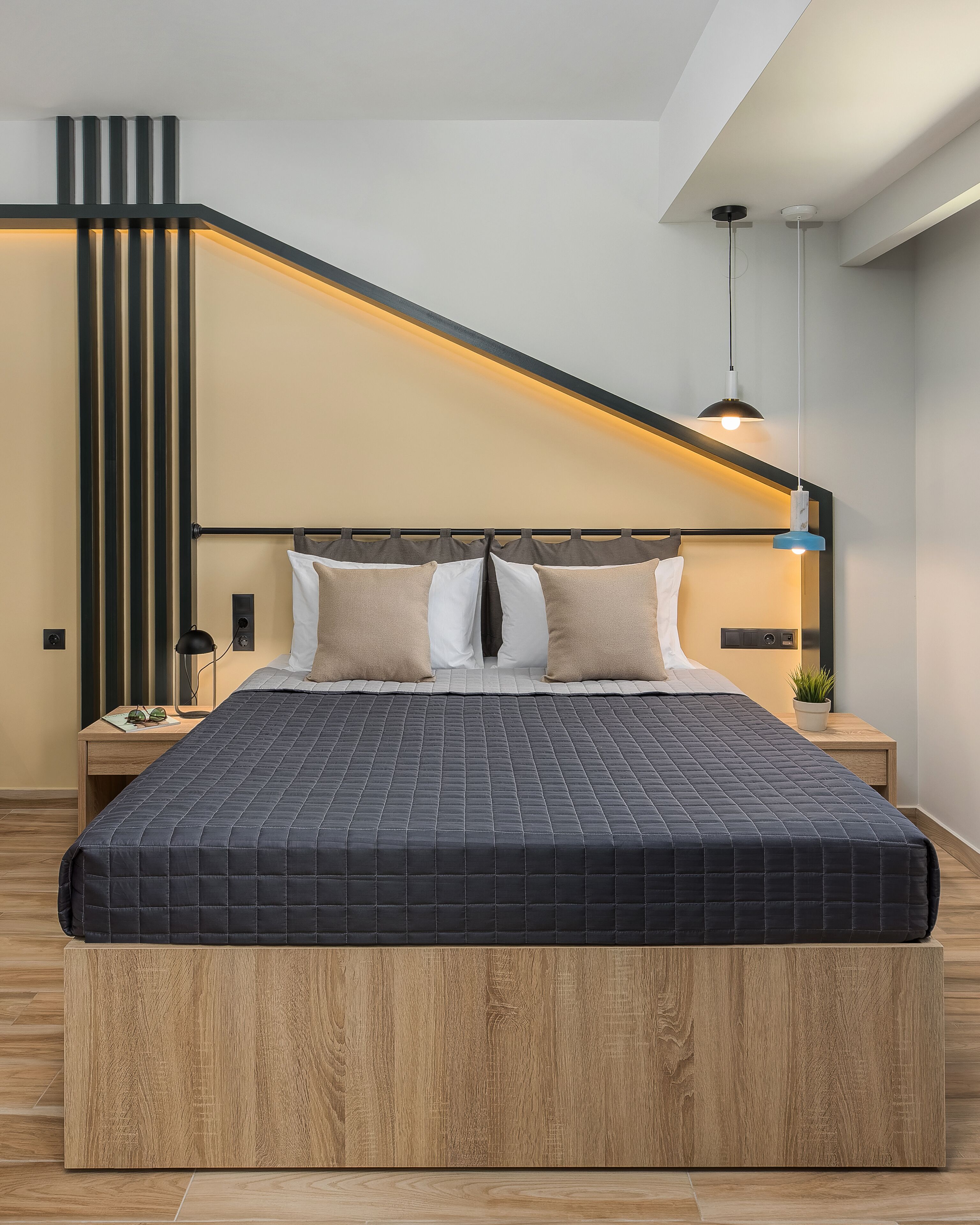 A modern bedroom with a large bed, a wooden headboard, a bedside table with a lamp, and a wall-mounted light fixture.