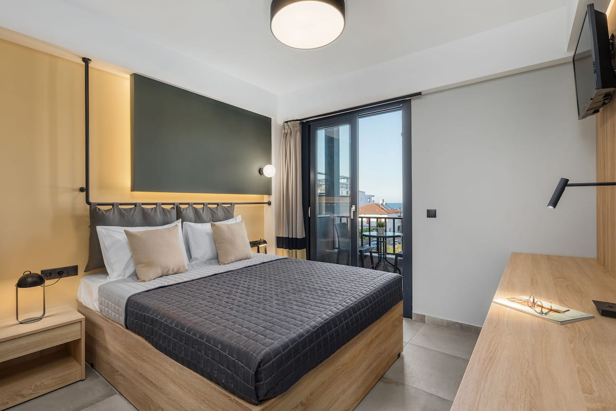 A modern hotel room with a large bed, a desk, and a balcony with a city view.