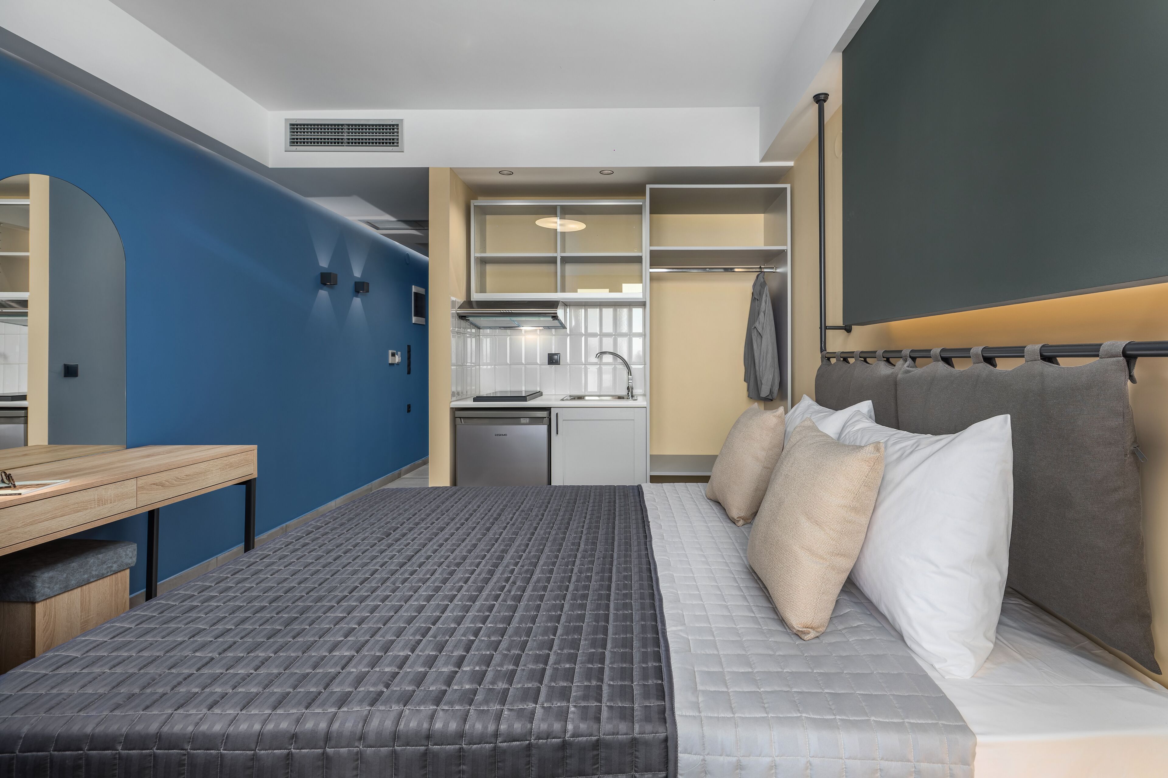 Quarto de hotel moderno com cama, escrivaninha e cozinha compacta.