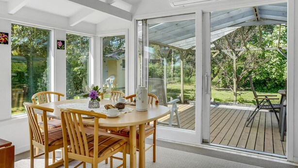 Una habitación luminosa con una mesa y sillas de madera, ventanas amplias y vista a un jardín.