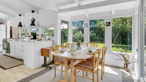 Una cocina moderna con muebles blancos, una isla central y un comedor con sillas y mesa de madera.