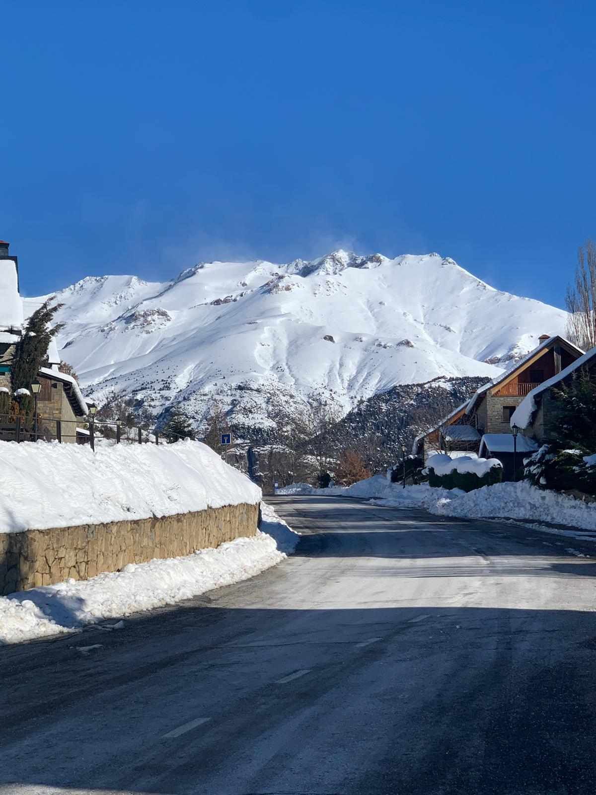 Carretera nevada en la montaña, con edificios a ambos lados.