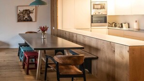 Une cuisine moderne avec des meubles en bois, un four encastré et un coin repas comprenant un banc et des tabourets.