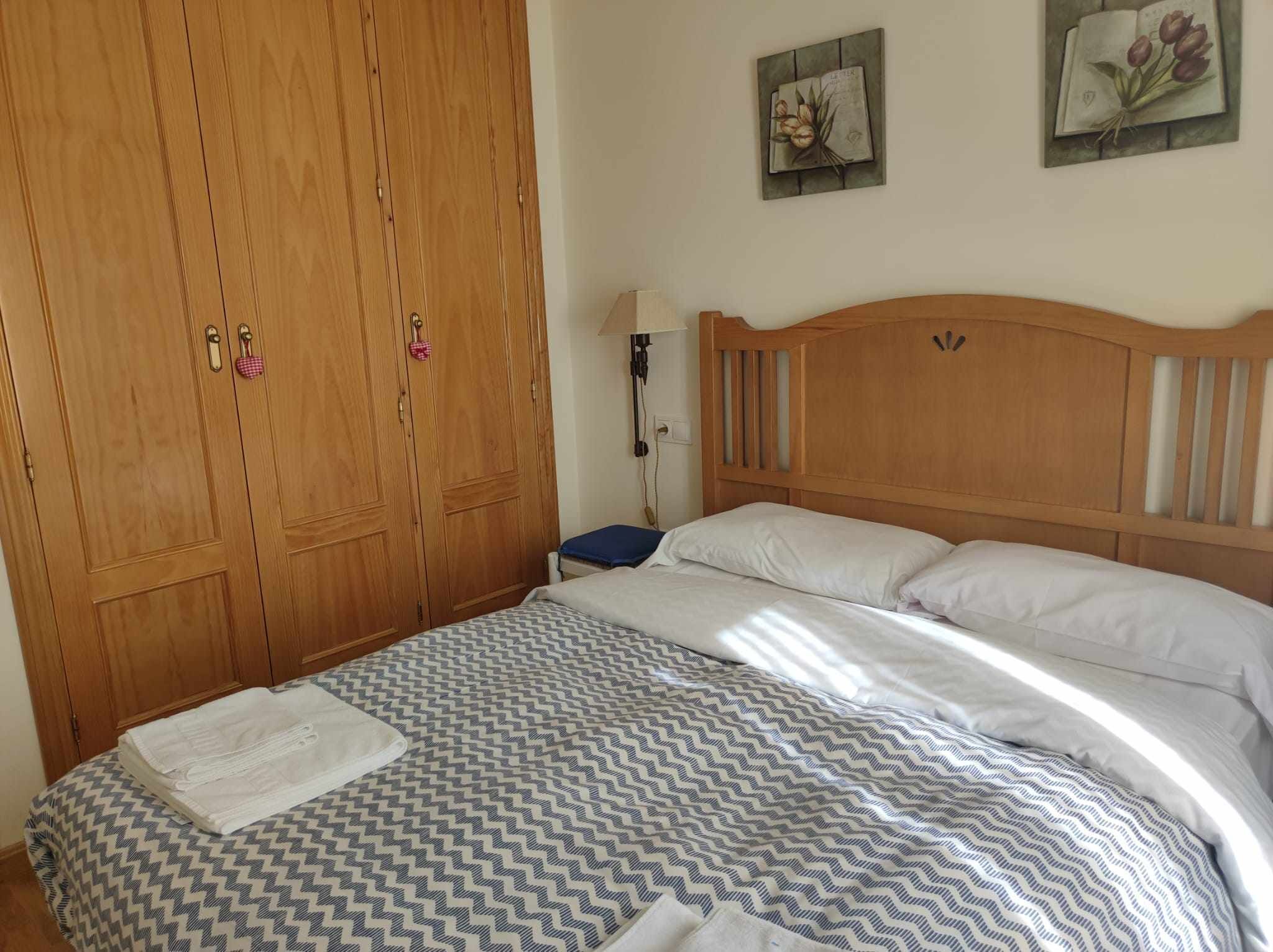 Quarto com guarda-roupa de madeira, cama com roupa de cama estampada e dois quadros na parede.