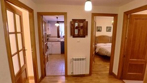 Un pasillo estrecho conduce a un dormitorio con cama y radiador. Se ve una cocina con fregadero y lavadora a través de una puerta abierta.