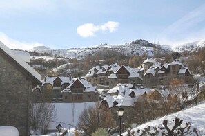 A snow-covered village with traditional wooden houses, a stone building, and a street lamp.
