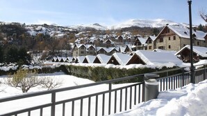 Ein schneebedecktes Dorf mit traditionellen Chalets, ein Steinhaus mit Holzfassade und eine Straßenlaterne.