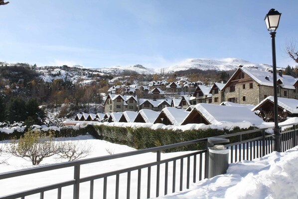 A snow-covered village with traditional chalet-style buildings, a clear sky, and a mountain in the background.