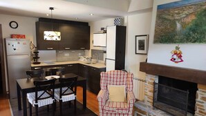 Een moderne keuken met donkere kastjes, een eethoek met een tafel en stoelen, en een open haard met een stenen omlijsting.