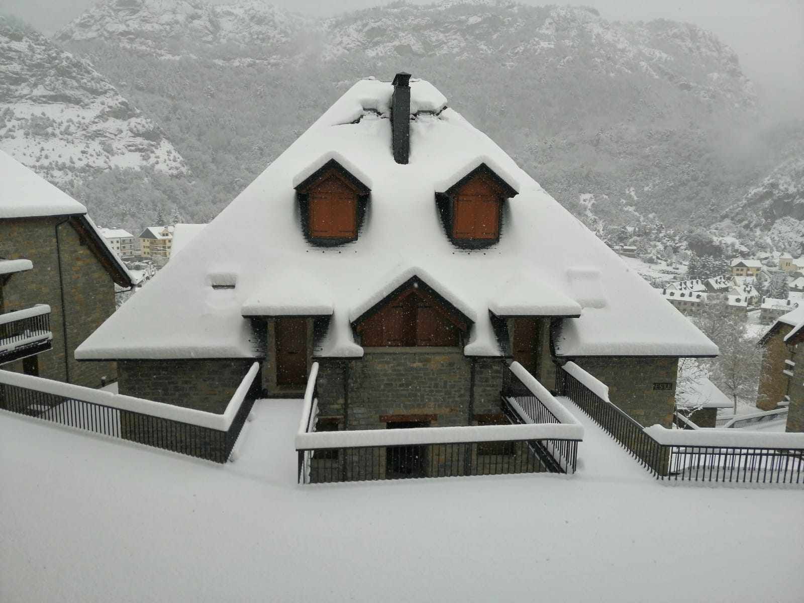A snow-covered building with a steep roof and wooden windows, surrounded by a snowy landscape.