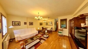 Una sala de estar con sofá, mesa de comedor, sillas, una araña y televisor.