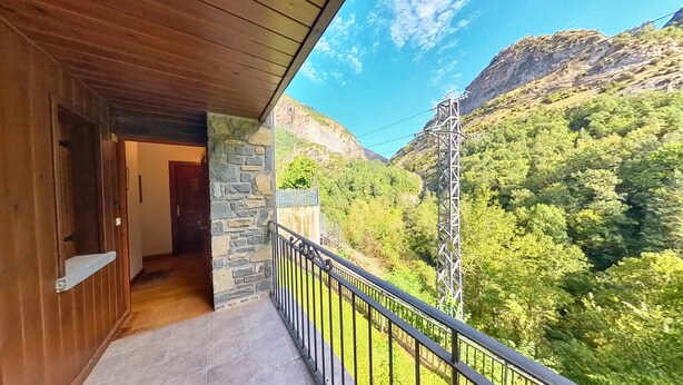 Un balcón de madera con muros de piedra que da a un valle exuberante y montañas.
