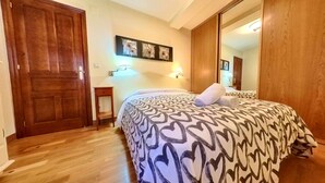 Habitación de hotel con una cama grande, una puerta de madera, una mesita pequeña y una lámpara fijada a la pared.