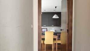 A hallway leading to a kitchen with wooden flooring, a dining table with chairs, and a pendant light.
