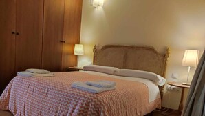 A hotel room with a large bed, two bedside tables, a wooden wardrobe, and a green armchair.