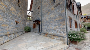 A stone building with a sign reading "OESTE" and a small garden area with pink flowers.
