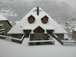 A snow-covered building with a steep roof and wooden windows, surrounded by a snowy landscape.