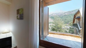 Ein Zimmer mit großem Fenster und Blick auf eine gebirgige Landschaft sowie ein Gebäude mit Holzfassade.