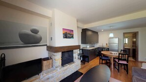 A modern kitchen with a stone fireplace, a dining area with a round table, and a living room with a sofa.