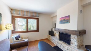 A living room with a stone fireplace, a large window with a view of a forest, a sofa, and a television.
