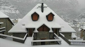 A snow-covered building with a steep roof and wooden windows, surrounded by a snowy landscape.
