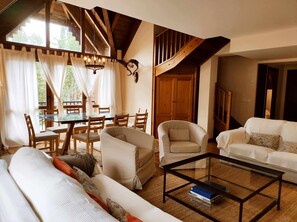Ein gemütliches Wohnzimmer mit einem Glastisch, zwei Sofas, einem Esstisch mit Stühlen und einer Treppe, die zu einer oberen Ebene führt.