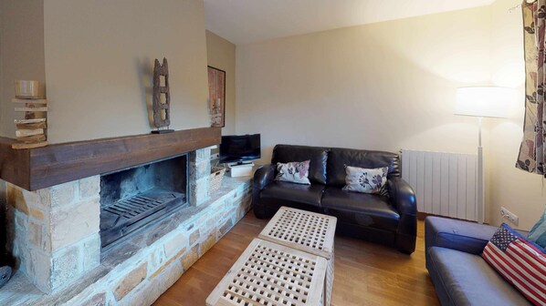 Una sala de estar con chimenea de piedra, un sofá de cuero negro y una mesa de centro de madera.