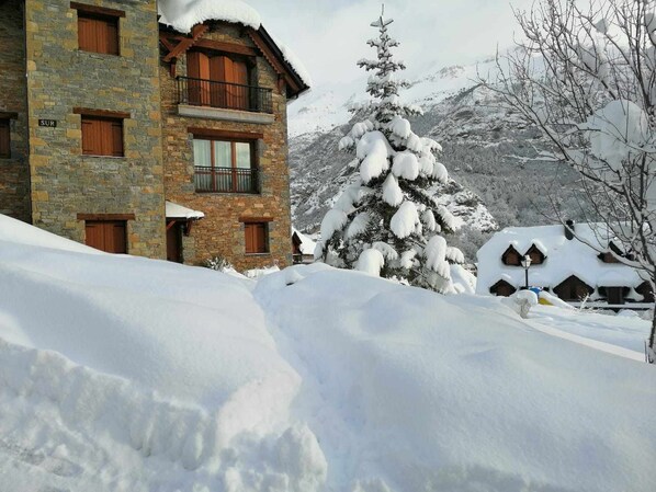 A stone building with multiple windows and balconies, surrounded by snow-covered trees and mountains.