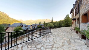 A stone-paved courtyard with a metal railing, surrounded by buildings with stone walls and wooden shutters.