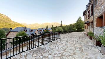 Un patio empedrado con barandilla de metal, rodeado de edificios con muros de piedra y contraventanas de madera.