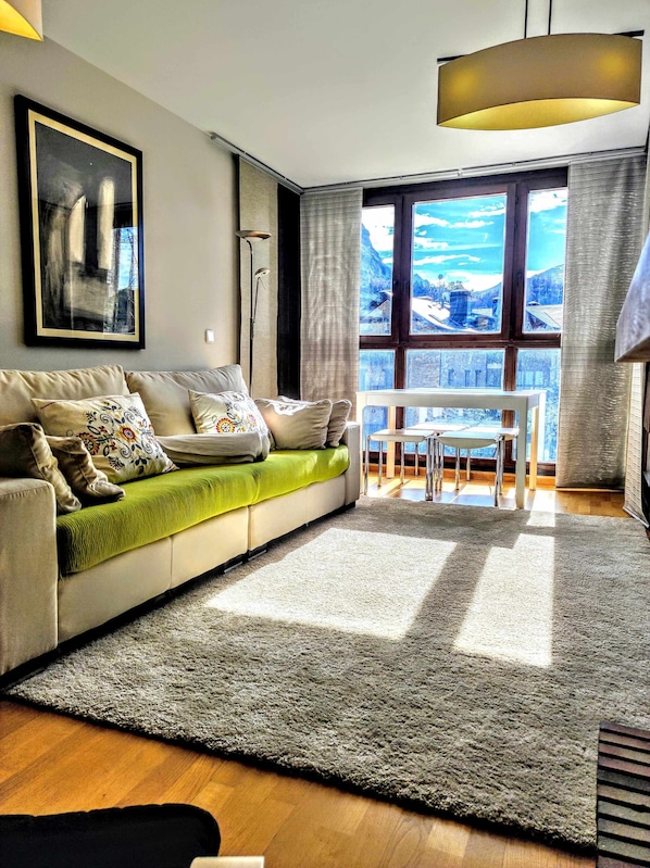 A modern living room with a sofa, a dining table, and a large window offering a view of mountains.