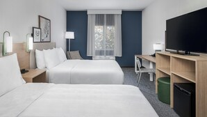 Une chambre d’hôtel avec deux lits, un bureau, une télévision et une fenêtre avec des rideaux.