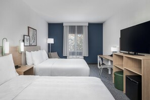 Ein Hotelzimmer mit zwei Betten, einem Schreibtisch, einem Fernseher und einem fensterbepflanzten Fenster.