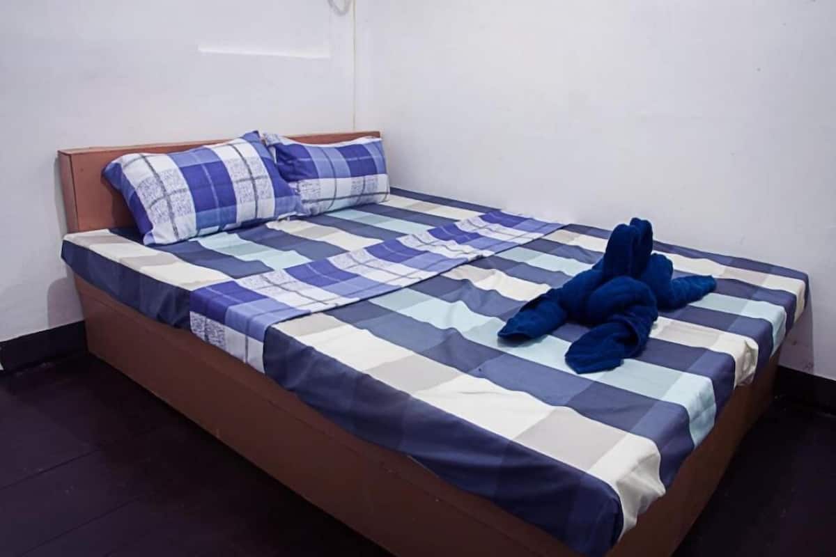 Una cama individual con una colcha a cuadros y dos almohadas, una con estampado azul y blanco y la otra lisa.