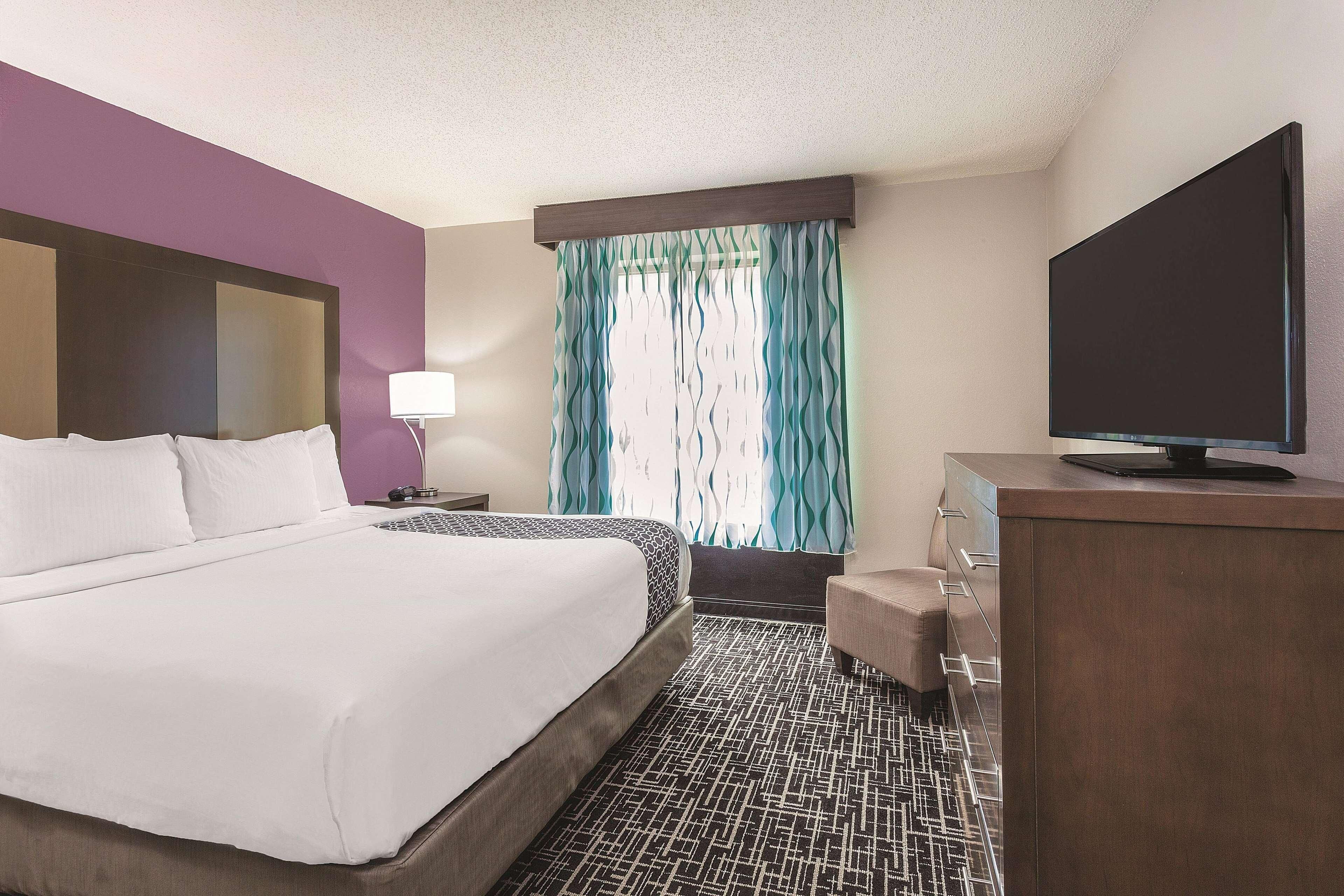 A hotel room with a large bed, a TV, a desk, and a window with curtains.