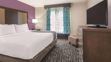 A hotel room with a large bed, a TV, a desk, and a window with curtains.