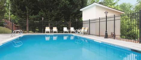 Una piscina con sillas de descanso y una cerca, rodeada de árboles.